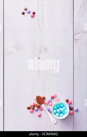 Colorful chocolate candies and a spoon of cocoa on a rustic white wooden table. Stock Photo