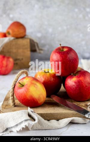 Red apples arranged on a rustic wooden table with fabric, styled as autumn harvest and fresh fruit concept. Stock Photo