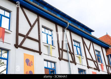 Modern building with blue-framed windows, half-timbered design, and colorful banners, vibrant architectural detail under cloudy sky. Stock Photo