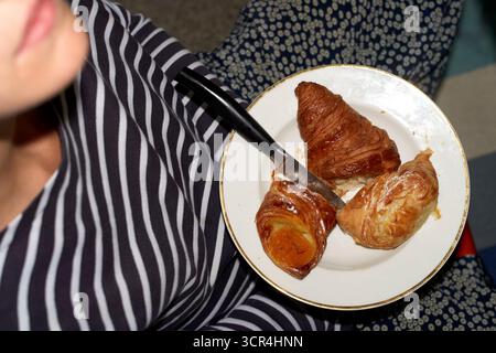 Woman holding a plate with three croissants and a knife on their lap. Stock Photo