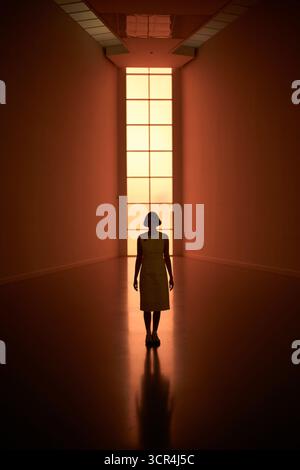 Woman standing in dimly lit hallway with glowing tall window in the background. Germany Stock Photo