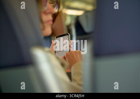 Woman in glasses using a smartphone while traveling on a train or bus. Brussels, Belgium Stock Photo