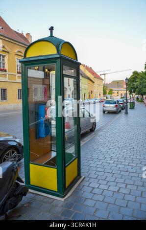 Budapest, Hungary – July 10, 2017: Traditional vintage phone booth with yellow and green colors on a cobblestone street. Stock Photo