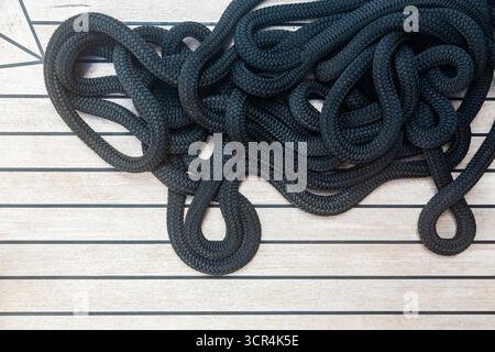 Neat pile of black sailing rope on a wooden teak deck of a luxury yacht, top view, close up Stock Photo