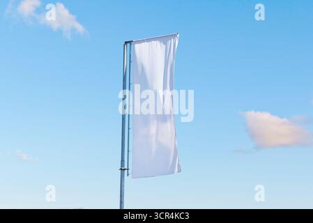 Vertical white advertising flag on metal pole fluttering in wind under clear blue sky, minimal promotional template Stock Photo
