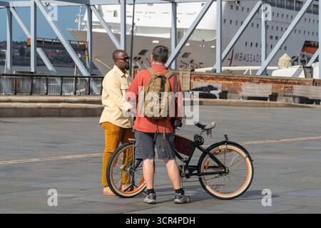 Two men, one black and one white with a bicycle, chatting on the promenade at Albert Dock, Liverpool, UK Stock Photo