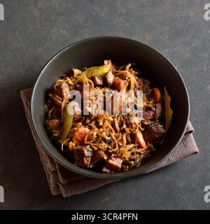 Traditional polish Bigos in bowl on dark stone background. Stewed cabbage with sauerkraut, mushrooms, smoked meats and spices. Close up view Stock Photo