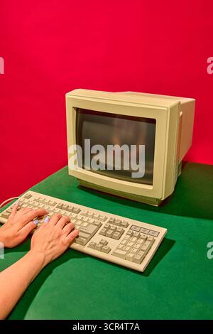 Hands typing on retro beige keyboard with emotional focus under vivid red background Stock Photo