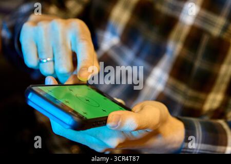 Closeup of man using his smartphone indoors while wearing plaid clothing and engaging with digital apps Stock Photo