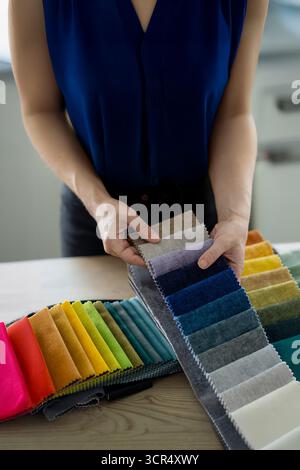 Female hands browsing fabric swatches in an upholstery showroom or artisan workshop. Concept of upholstery, home renovation, interior design Stock Photo