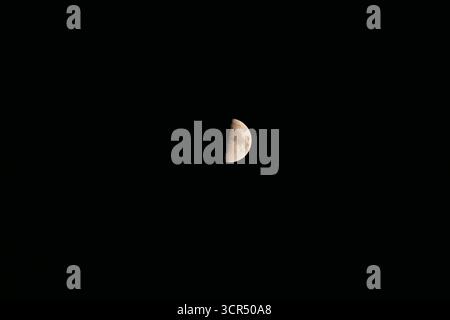 A half moon illuminated against a dark night sky. The moon displays a thin, bright edge with a shadowed portion visible. Stock Photo