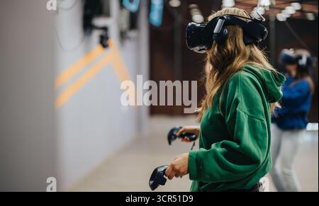 Young women enjoying an immersive virtual experience using VR headsets and controllers in a modern gaming center or arena. Stock Photo