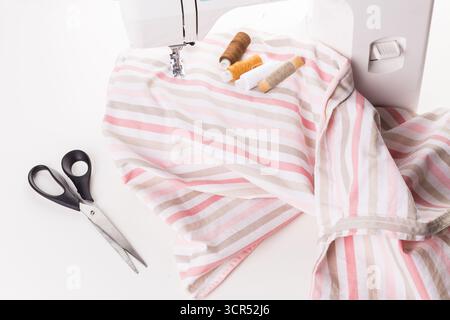 Sewing a striped fabric with scissors and threads on a sewing machine at home Stock Photo