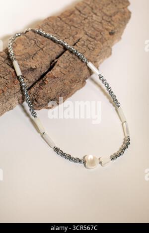 A beautiful costume jewelry necklace rests on a piece of textured wood. It features silver beads mixed with white accents, creating a stylish and eye- Stock Photo