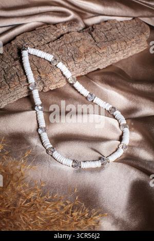 A stylish necklace made of colorful beads and clear pendants is elegantly arranged on a smooth silk fabric. The contrast with the wooden texture adds Stock Photo