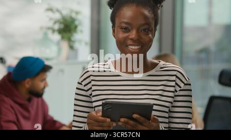 Portrait African American casual businesswoman typing digital tablet online app looking at camera smiling informal business woman female girl in Stock Photo