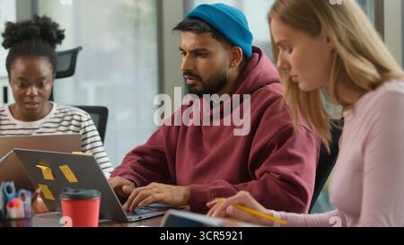 Three concentrated informal business diversity people together team focused indoor in office Indian pensive man with laptop thinking Caucasian female Stock Photo