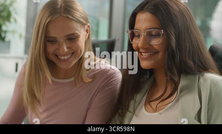 Two diversity business women in coworking company office laughing smiling talking communicate using computers laptops cooperation job multiracial Stock Photo