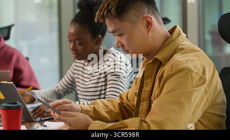Informal collaboration in office project business at table working cooperate three multiethnic colleagues Asian male with digital tablet African Stock Photo
