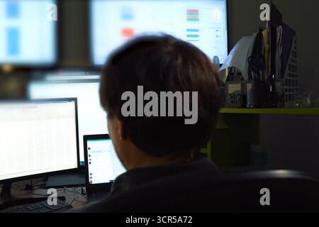 The hacker sits behind the monitor and works. The work of computer technician and programmer. Stock Photo