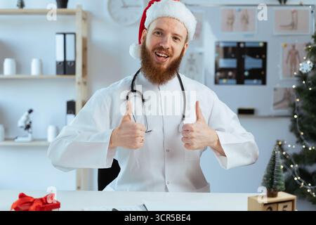 Bearded Doctor on the shift showing positive likes gesture with thumbs-up, while working on Christmas eve. copy space Stock Photo