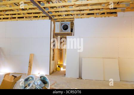 Workers are installing drywall in large room, with exposed framing, tools scattered around construction site. Stock Photo