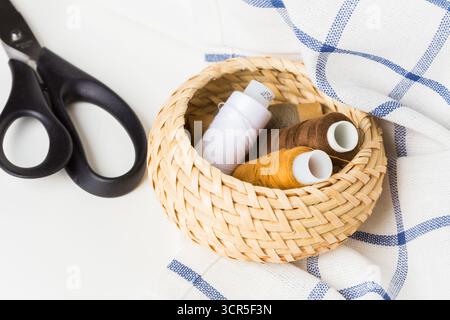 Sewing supplies arranged in a woven basket with scissors on a fabric Stock Photo