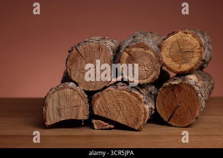 Pile of cut firewood on wooden table against brown background, closeup Stock Photo