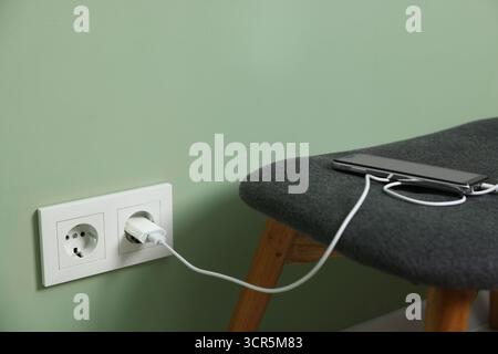 USB adapter with cable plugged into electric socket charging smartphone indoors Stock Photo