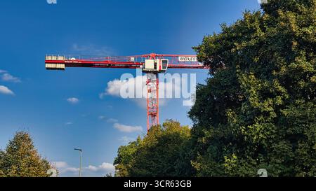 Red tower construction crane against blue sky and green trees during urban building project Stock Photo