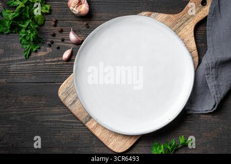 Empty white plate with herbs, spices and garlic on dark wooden background, top view, copy space. Serving plate mockup. Food background, design templat Stock Photo
