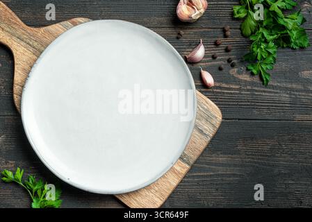 Empty white plate with herbs, spices and garlic on dark wooden background, top view, copy space. Serving plate mockup. Food background, design templat Stock Photo
