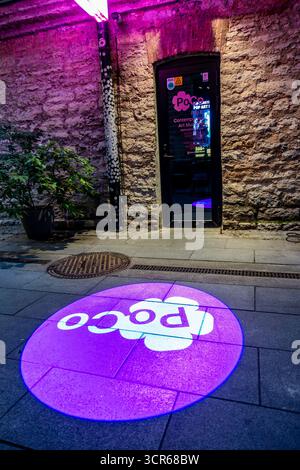 Entrance to PoCo Pop and Contemporary Art Museum in Tallinn, Estonia, with illuminated purple logo projection on pavement and stone wall background. Stock Photo