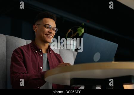 Smiling young businessman in smart casual working on laptop in office lounge Stock Photo