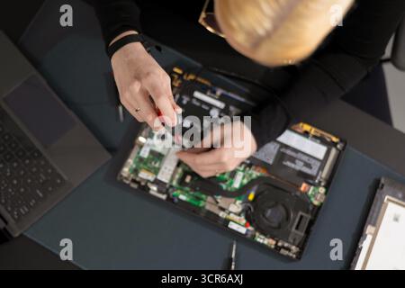 Female IT technician repairs laptop motherboard with screwdriver during maintenance and upgrade session Stock Photo