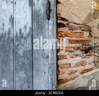 Rustic old wall with peeling plaster, exposed red bricks, and faded antique door. Perfect grunge textured background with copy space. Stock Photo