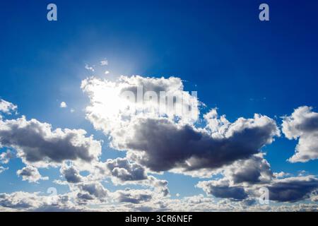 Bright sun peeking through fluffy white clouds in a vibrant blue sky with scattered different shaped clouds in the atmosphere from Roker Pier Stock Photo