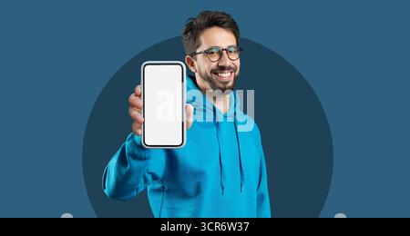 Man in Blue Hoodie Holds Smartphone, Showcasing Screen With a Friendly Smile, Suitable for Advertising or Promotional Use Stock Photo