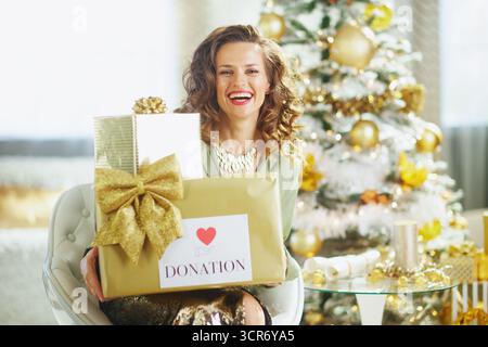 A smiling woman with curly brown hair holds two beautifully wrapped gold gift boxes, one clearly labeled DONATION, symbolizing generosity during the f Stock Photo
