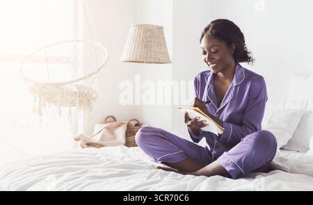Black Female Taking Notes Writing In Notebook Sitting In Bedroom Stock Photo
