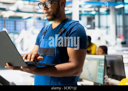 Black engineer testing solar technology in renewable energy facility on pc, focusing on software troubleshooting and performance metrics. Eco friendly industrial operations on laptop. Stock Photo