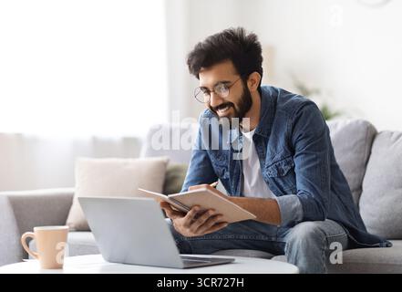 Distance Learning. Indian Man Study With Laptop At Home And Taking Notes Stock Photo
