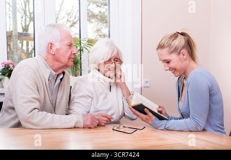 carer reading a book to an elderly couple Stock Photo