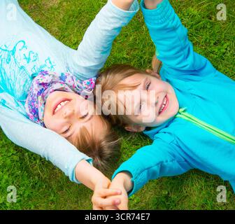 two girl friends lie on the meadow and hold hands Stock Photo