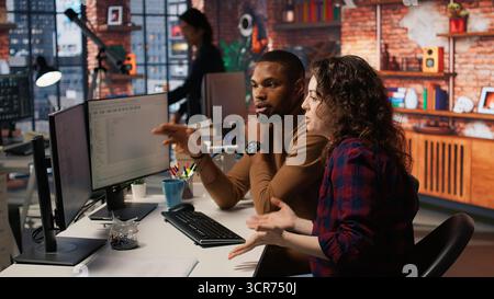 Engineers cooperating in startup office, using programming languages on PC to build applications. Coworkers doing brainstorming, using computer in software development agency to code, camera A Stock Photo