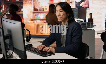 Portrait of smiling senior engineer coding advanced AI algorithm in startup office, refining machine learning models. Cheerful man using coding platform in Silicon Valley workplace, camera A Stock Photo