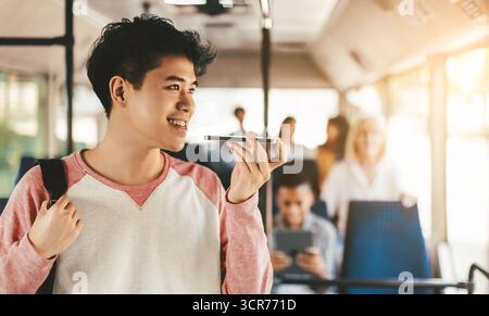 Young Man Using Voice Assistant on Bus While Other Passengers Relax Stock Photo