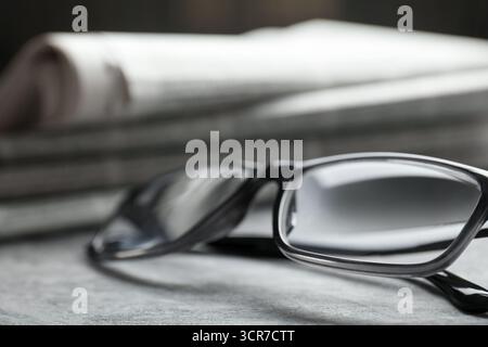 Stack of newspapers and glasses on grey table, closeup Stock Photo