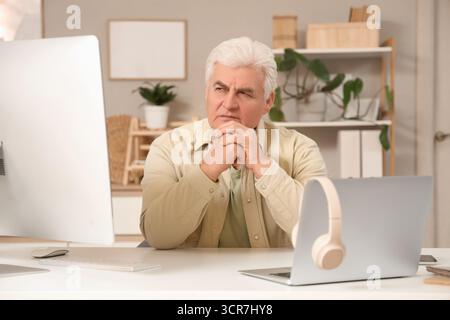 Thoughtful senior programmer working at desk in office Stock Photo