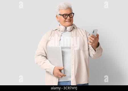 Senior programmer with laptop and mobile phone on light background Stock Photo